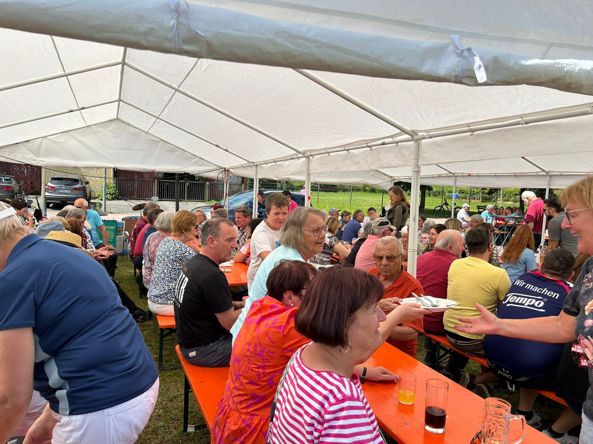 Der Blick geht durch den aufgestellten Pavillion unter dem viele Gäste an Bierbänken sitzen.